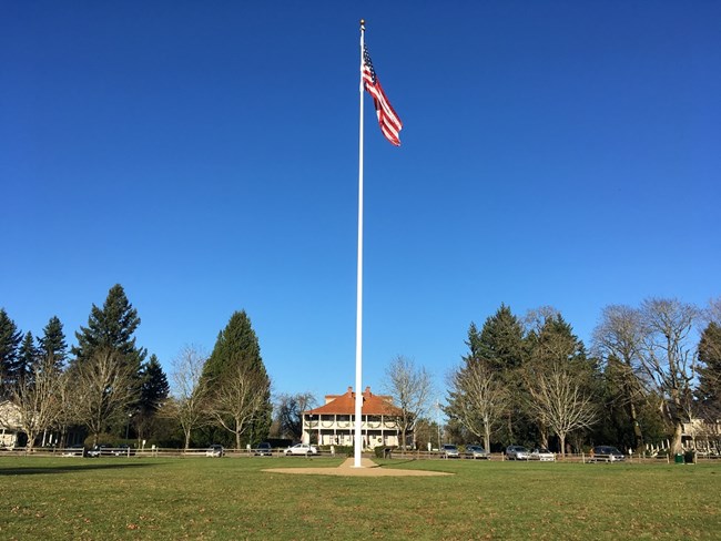 An American flag flies on the Parade Ground flagstaff on a clear day. Behind it is the Grant House on Officers' Row.