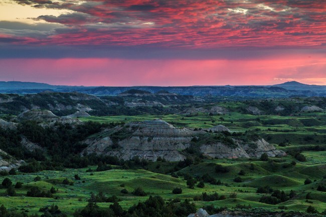 Pink and purple sky over rolling badlands terrain.