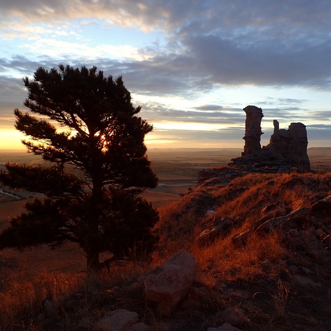 A glowing orange sky is silhouetted by distinctive rock towers.