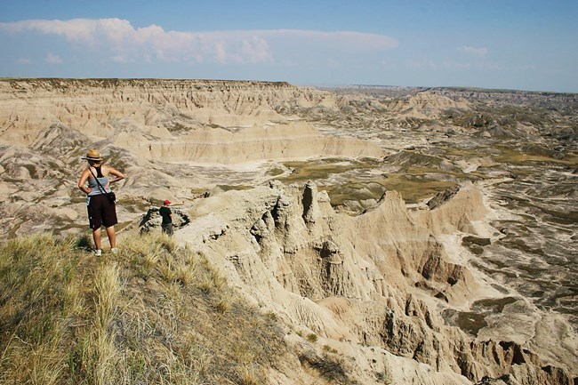 StrongHold_1 two hikers stand on the high point of a butte, looking down into badlands formations as they stretch toward the horizon