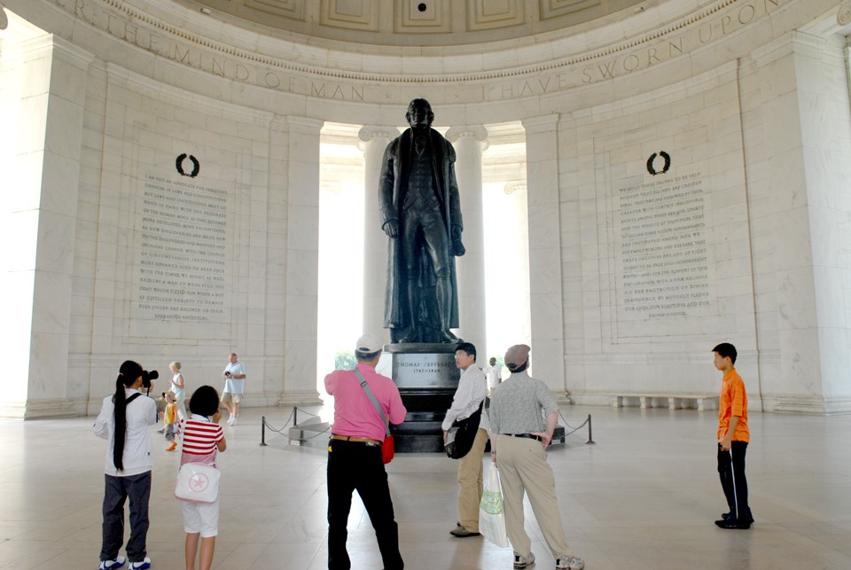 A group of adults and children take photos of a bronze statue of Thomas Jefferson