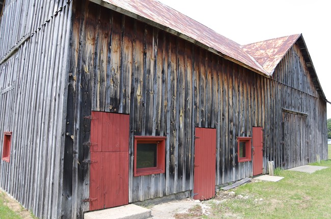 Wooden Barn with ribbed accents along the outside, door and window frames painted red.
