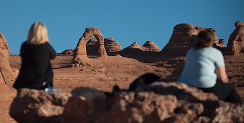 ARCHUpperViewpoint two people sit on a rock with a distant view of a stone arch