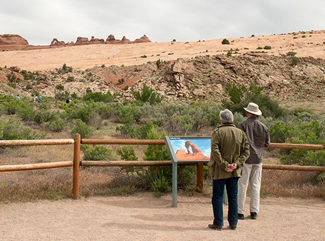 DAViewpoint two people stand near a sign with a distant view of Delicate Arch