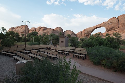 Skyline - Amphitheater a group of benches stands in front of an arch in a high wall.
