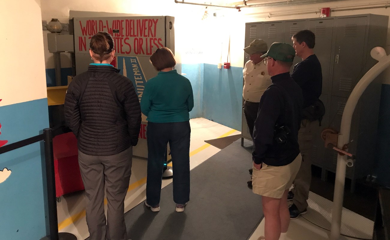 visitors stand in front of a large blast door in an underground space