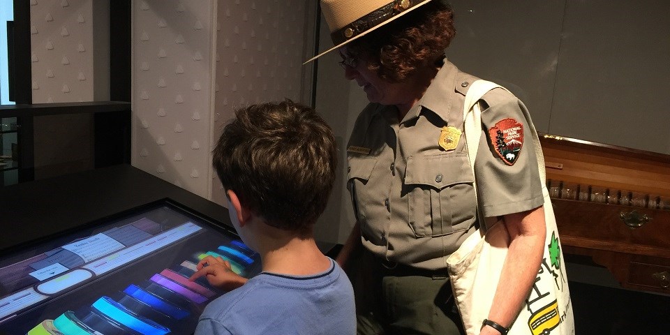 Color image of a child playing a virtual glass armonica on a computer screen as a ranger watches. Color image of a child playing a virtual glass armonica on a computer screen as a ranger watches.