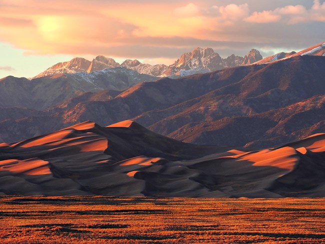 Tall dune and snow-capped mountains at sunset
