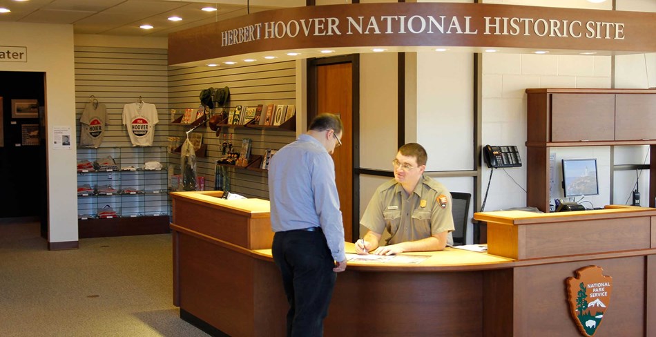 A ranger at an information desk assists a park visitor. A ranger at an information desk assists a park visitor.