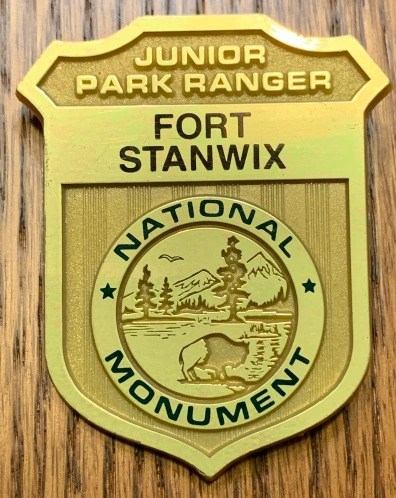 A shiny park ranger badge with the words: "Fort Stanwix National Monument Junior Ranger" embossed on it.