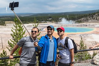 Three visitors take a selfie in front of a colorful hot spring.