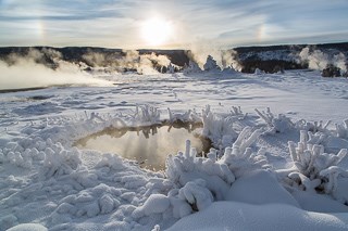 Geysers steam in the distance of a snow-covered landscape.