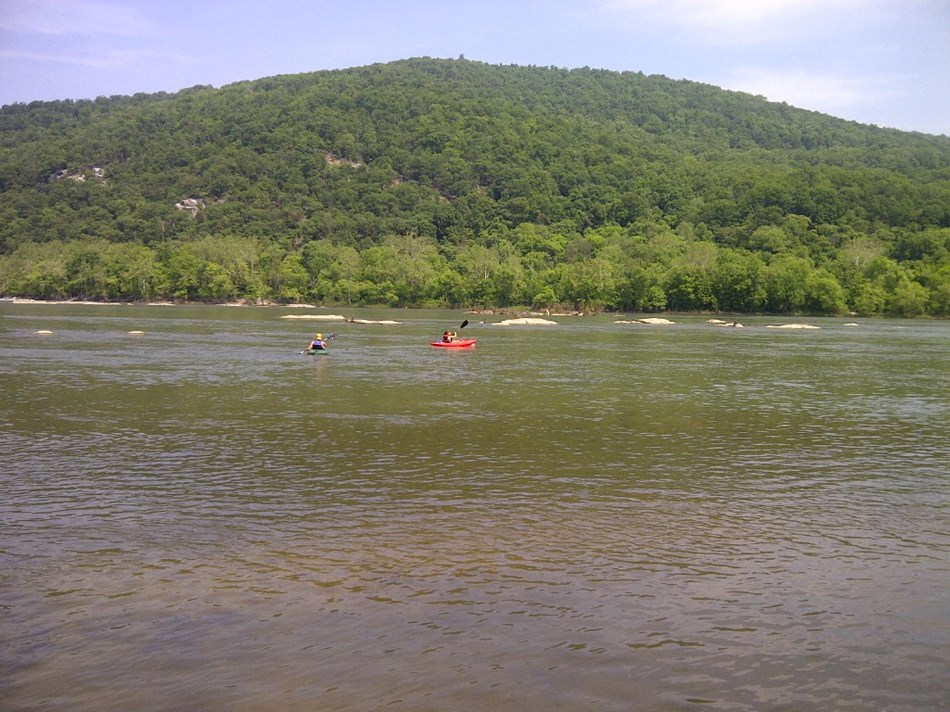 two kayers in a landscape of river, rocks and forested hills two kayers in a landscape of river, rocks and forested hills