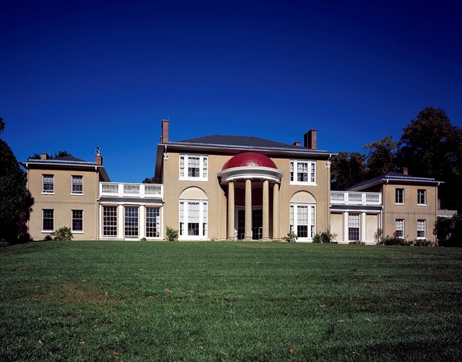 red dome Exterior of Tudor Place. tan walls with red domed porch. Green lawn in the foreground.