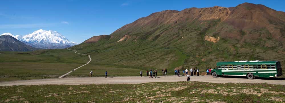 shuttle a bus parked with many people standing outside looking at a scenic landscape