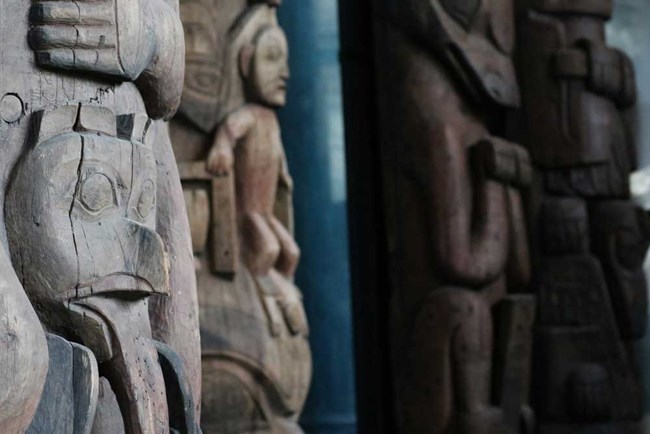 House posts displayed in Totem Hall closeup of several totem poles with carvings of humans, birds and other animals