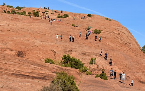 trail to delicate arch a bare rock slope with a line of people walking up it