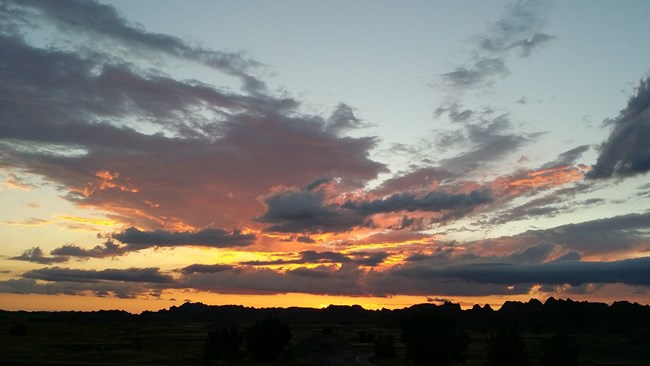 a cloudy sunset with swirls of orange, yellow, and pink and badlands buttes at the bottom