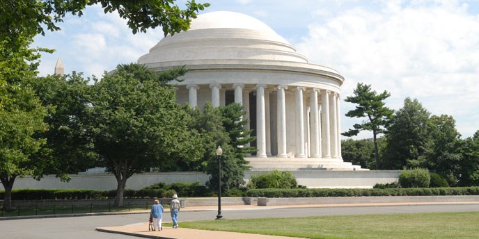 Trees and shrubs surround white Roman architectural style building