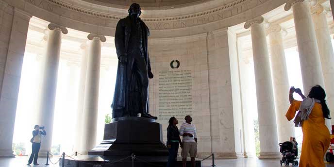 Bronze statue of man in coat on a pedestal in a chamber area with writing on the wall