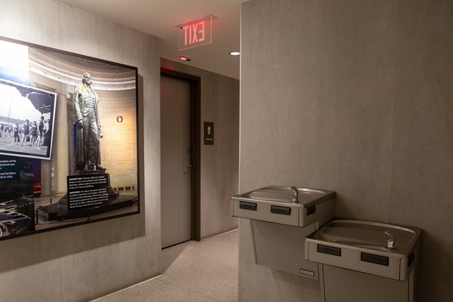 Two drinking fountains of different heights next to a door to a restroom.