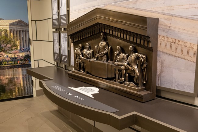 A bronze scale model of carved decorations around the outside of the memorial.