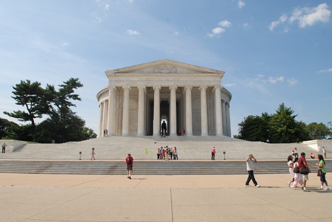Visitors on the wide stone steps leading up to the front of a large marble building lined with columns.