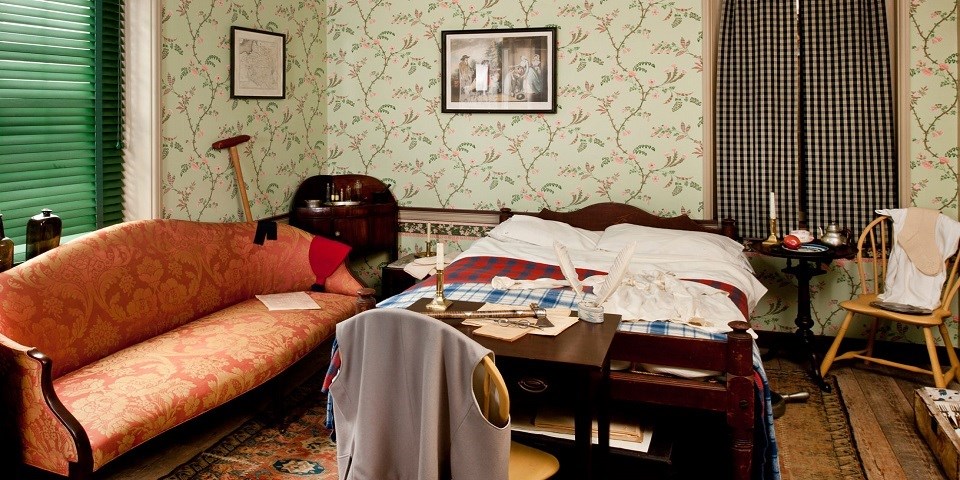Color photo of a recreated 18th-century bedroom with green floral wallpaper and wooden furniture. Color photo of a recreated 18th-century bedroom with green floral wallpaper and wooden furniture.