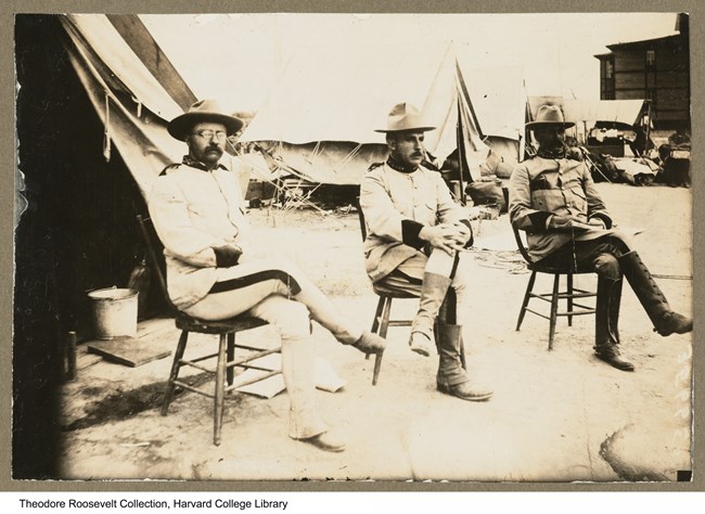 Image of three men sitting in front of tents in an encampment.