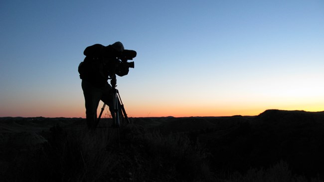 A man stands on the badlands while using a video recorder.