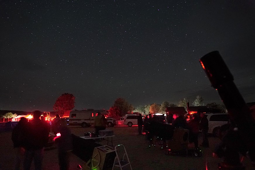stargazers gather in a field of telescopes lit by red lights to look up at the starry sky::Dakota Nights Telescope Field