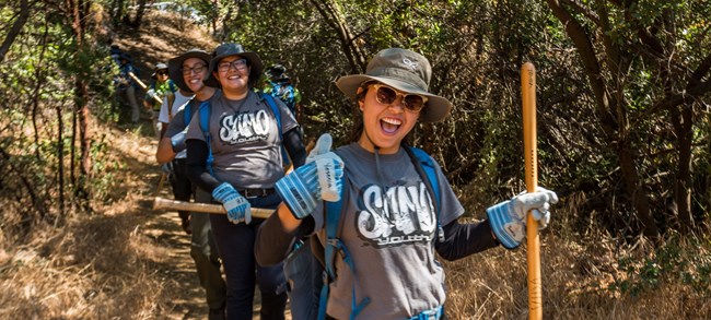 Volunteers with tools and work gloves smile at the camera while on a trail