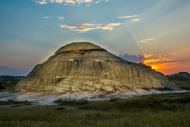 A butte stands alone backed by a sunset glow.
