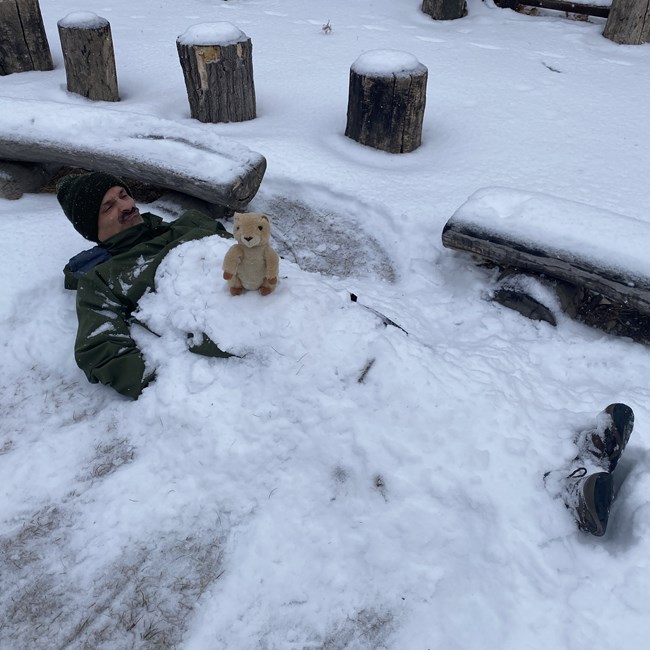 Ranger Peelee lays on the ground covered in snow, while a prairie dog plushie sits on top of him.