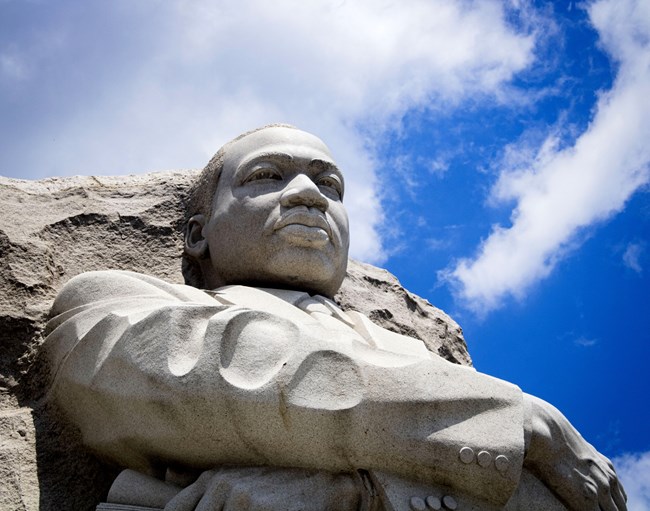 A statue of Martin Luther King Jr. in front of a blue sky.