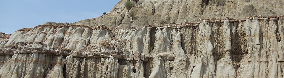 Horizontal layers of hard, rust-colored rock protect softer rock layers below which show signs of water erosion