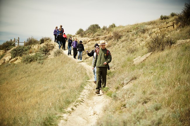 A Ranger leads several people down a trail towards the viewer