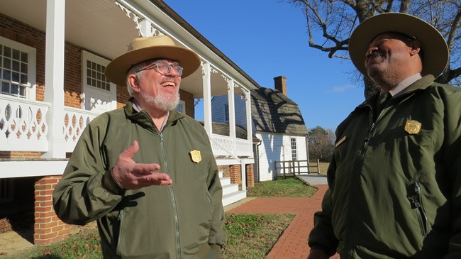 Two park rangers talking in front of the Thomas Stone House.