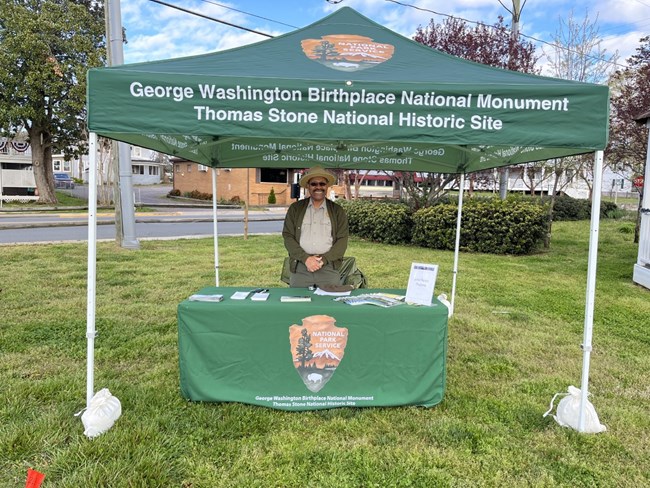 A park ranger standing at an outdoor booth which reads the park's name.