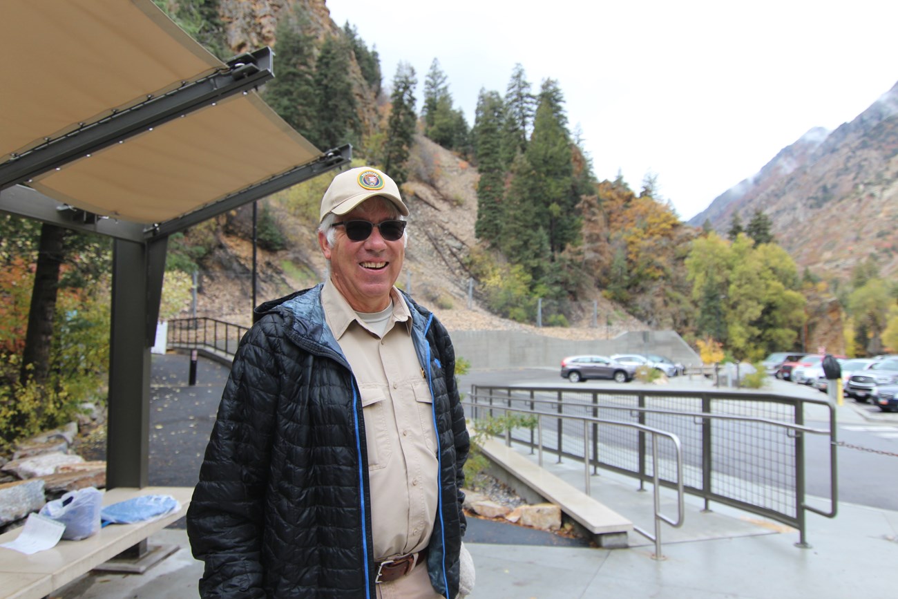 Volunteer standing on plaza with parking lot and trees in the background.