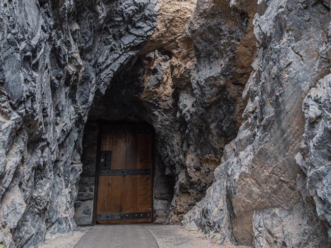 The Hansen Cave entrance door which is rectangular, wooden, and surrounded by rock.