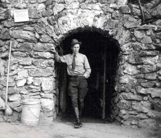 A ranger standing inside a rock arch. The image is black and white.