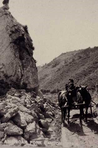 George Tyng sitting on the wagon with two horses at Split Rock, American Fork Canyon, trying to convince photographer CH Joy to get his son down from climbing on the rock.