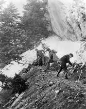 The Timpanogos Cave Committee sponsors the building of the trail to the caves which workers "carve" out of the cliffside. The three men pictured here are working with handtools to create a path.