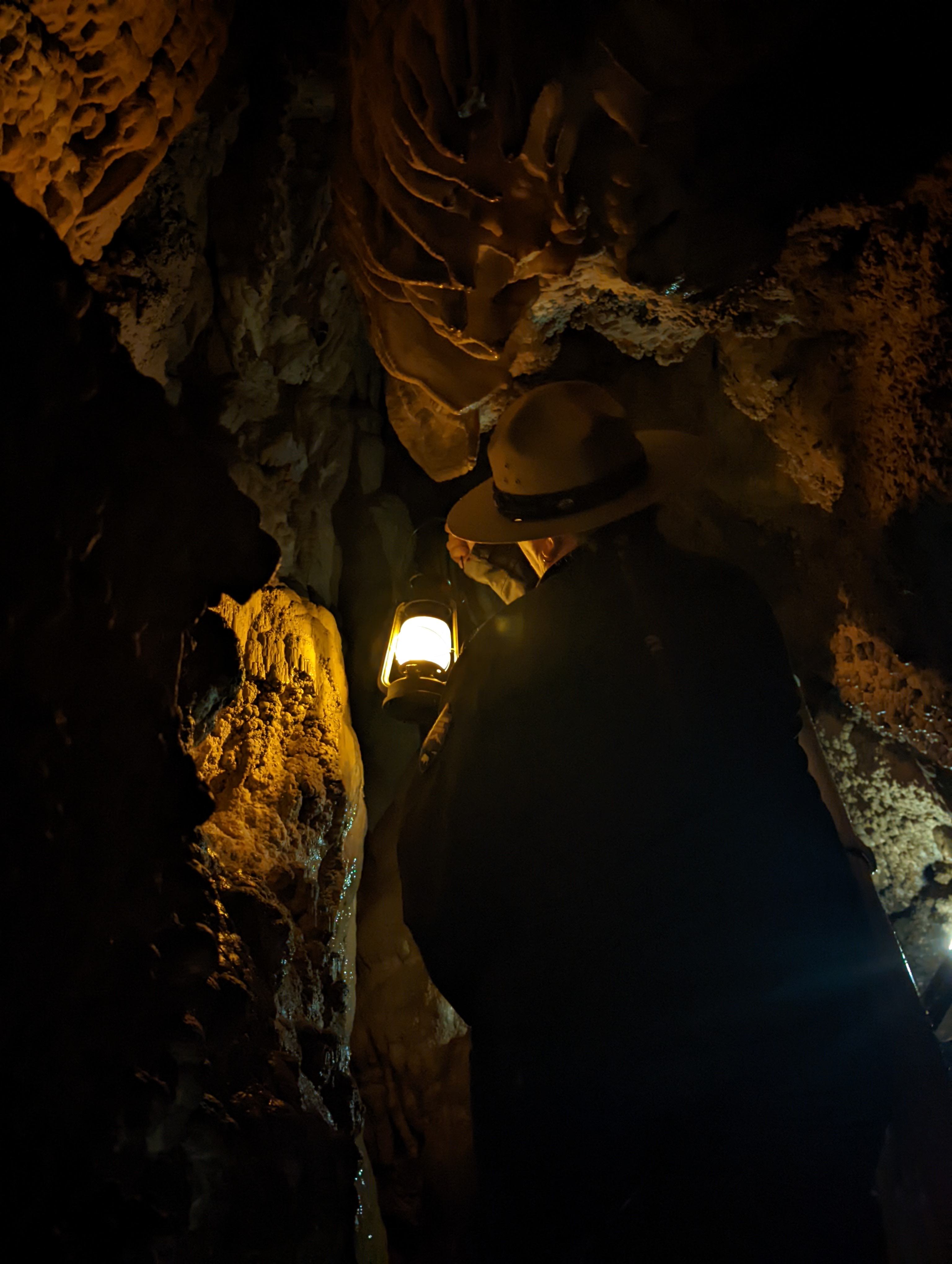 Ranger holds up a lantern, illuminating cave walls.