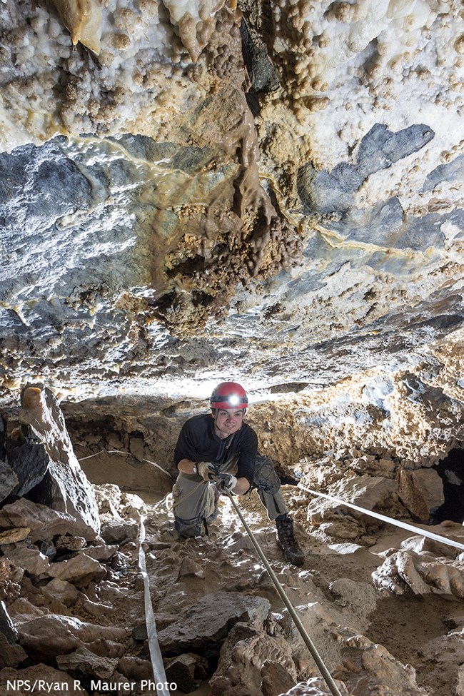 Rope in Hansen Cave Caver sits smiling while holds onto a rope handline in Hansen Cave, surrounded by rocks