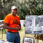 Cosmo historical society member stands next to historic cabin image