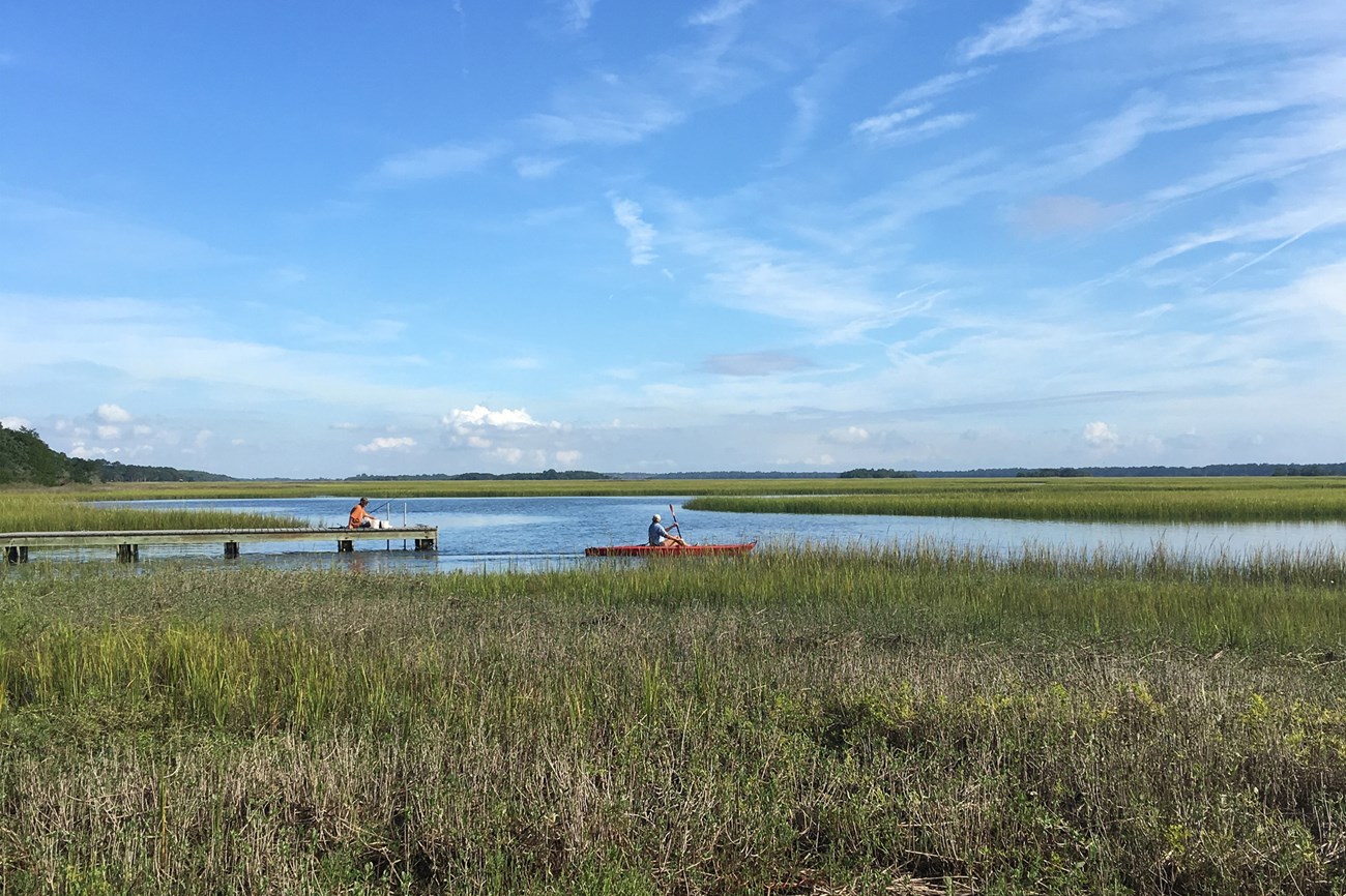Image of person fishing and person kayaking in salt marsh