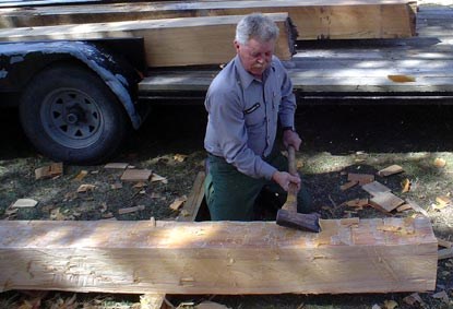 A preservation staff member is hewing a sill beam for the historic kitchen house.