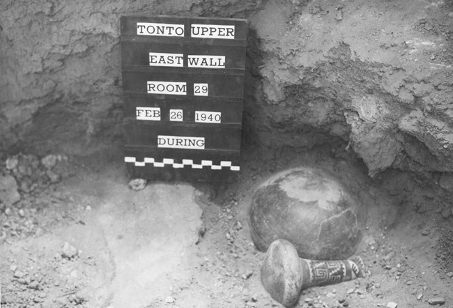 A black and white photo of two pieces of pottery in situ next to a board dated "FEB 26 1940".